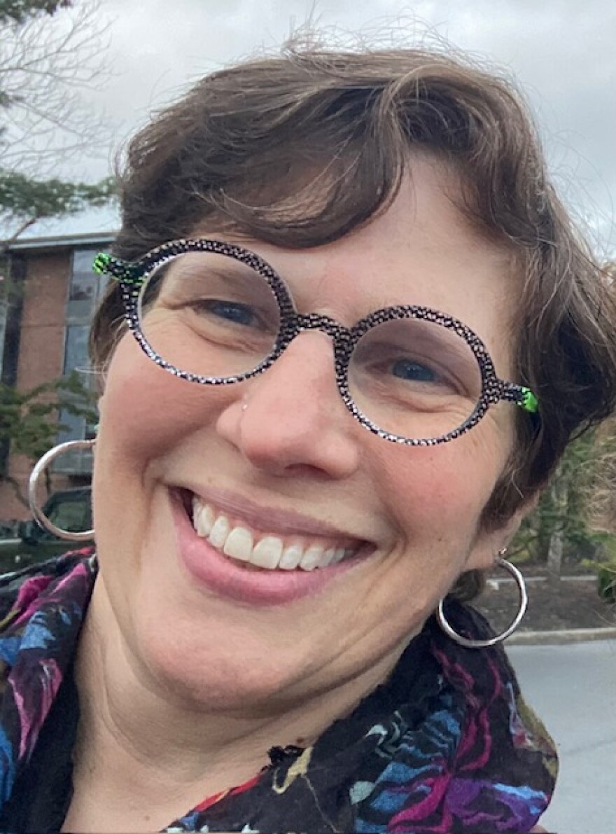 headshot of a smiling woman with short hair, round glasses and hoop earrings. 