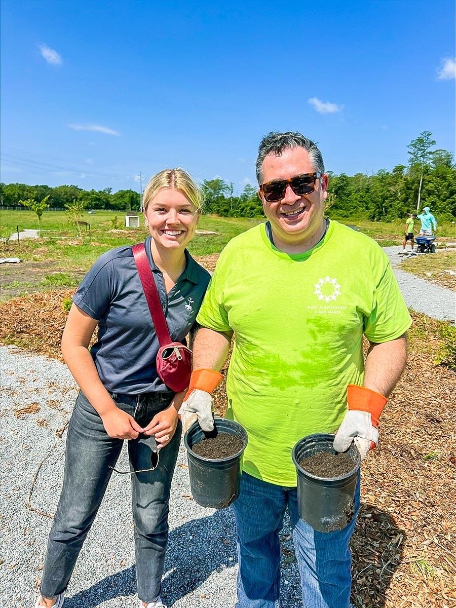 Two people stood next to each other smiling, the person on the right is holding two plant pots