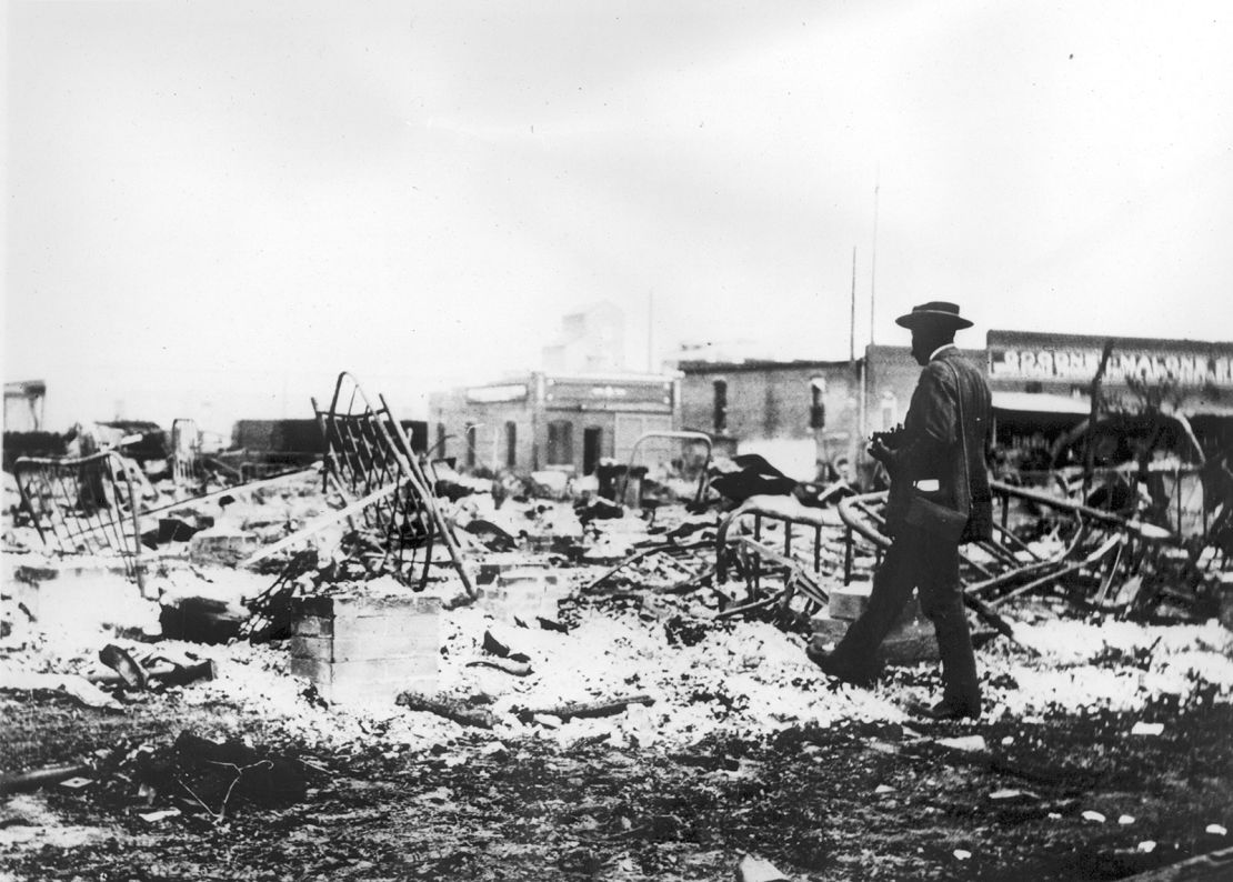 A Black man with a camera looking at the skeletons of iron beds which rise above the ashes of a burned-out block after the Tulsa Race Massacre in Tulsa, Oklahoma in June 1921.