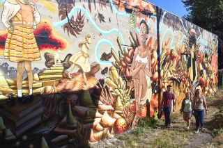 people walk past a colorful mural in an alley just off Northeast Alberta Street