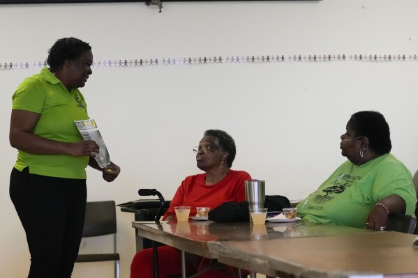 Krystal Martin, a Gloster native, shows pamphlets to residents Myrtis Woodard and Shelia Mae Dobbins, right, during a community meeting she organized regarding health complaints against the Drax facility in Gloster, Miss., Thursday, May 2, 2024. (AP Photo/Gerald Herbert)