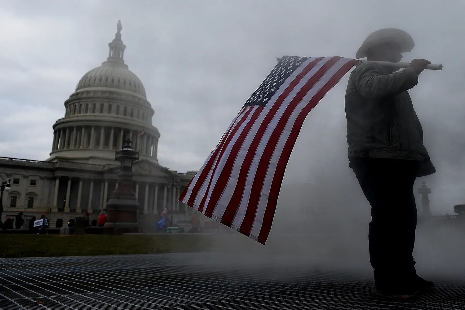 A protestor is seen outside the U.S. Capitol holding an American flag, surrounded by smoke.