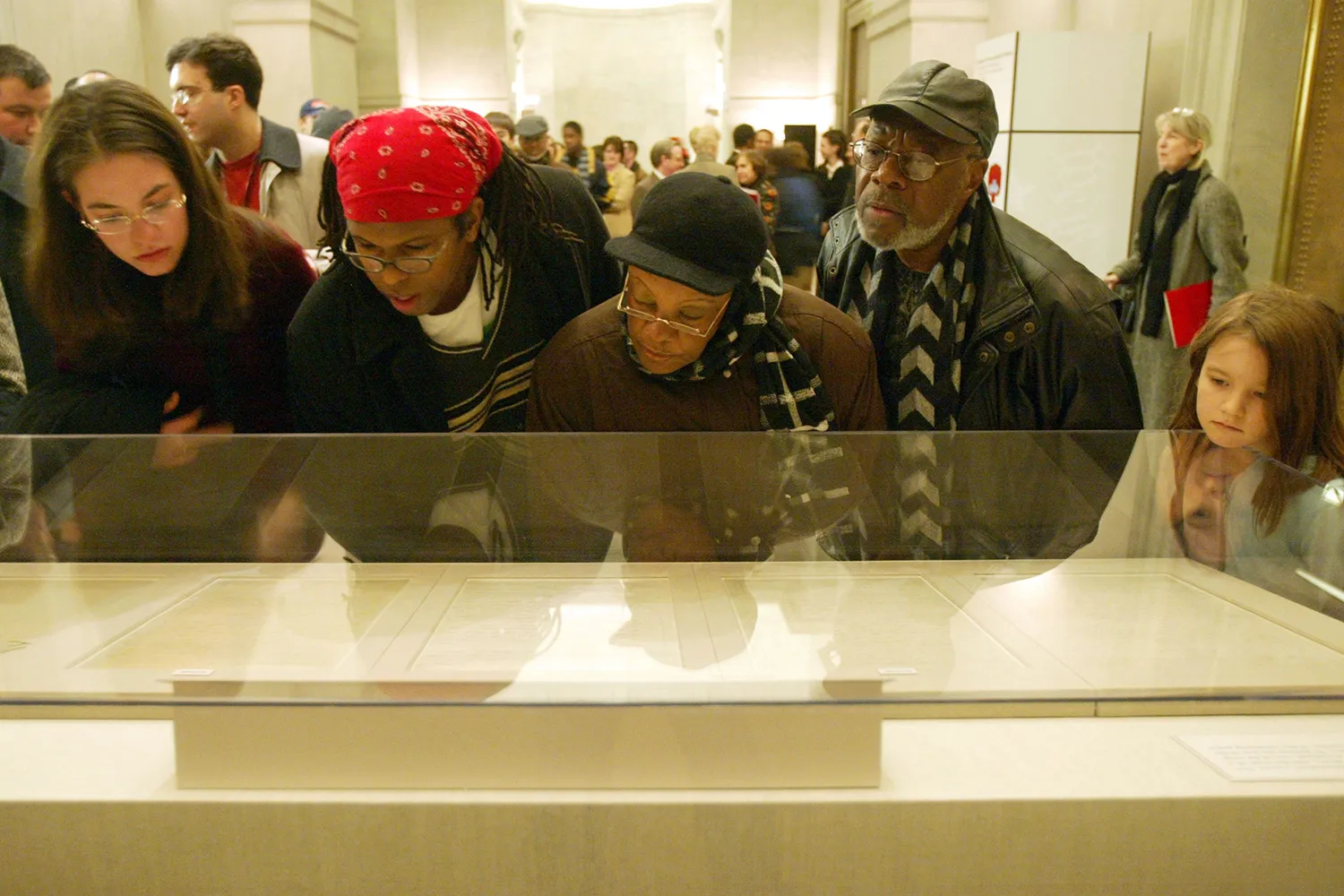 A group of five people lean in to a glass case to see the original Emancipation Proclamation.