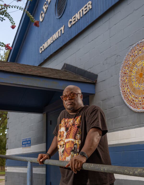 A man in glasses stands in front of a community center building.