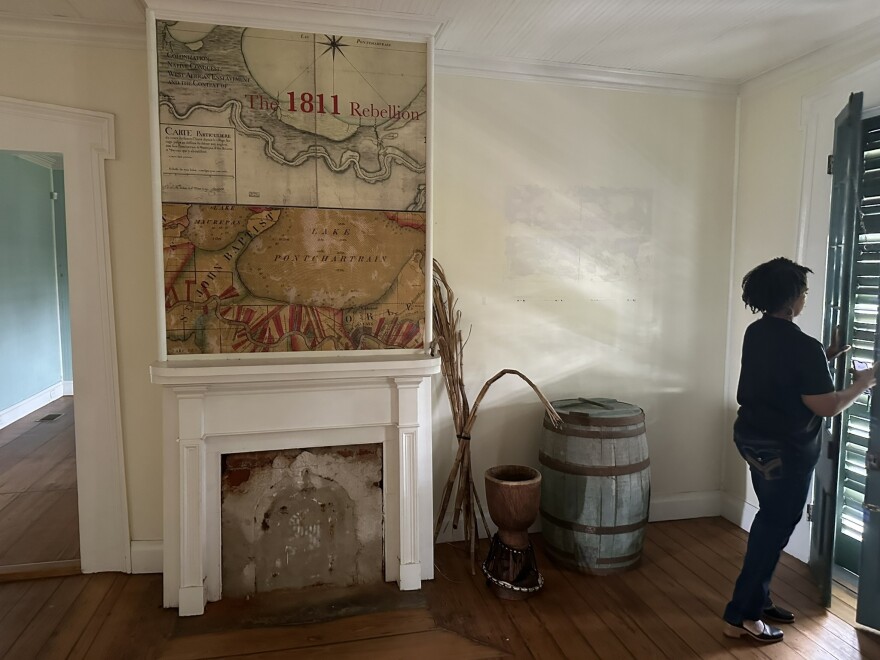 Jo Banner opens a shutter inside the plantation house. On the wall is a map showing the 1811 rebellion. 