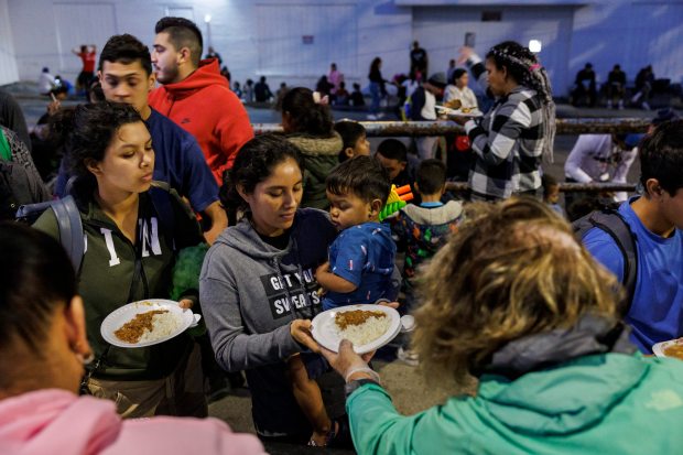 Migrants eat dinner outside a shelter on the Lower West Side, March 4, 2024 in Chicago. Several religious groups organized the event to feed migrants and hold a brief religious service on the sidewalk outside the shelter. (Armando L. Sanchez/Chicago Tribune)