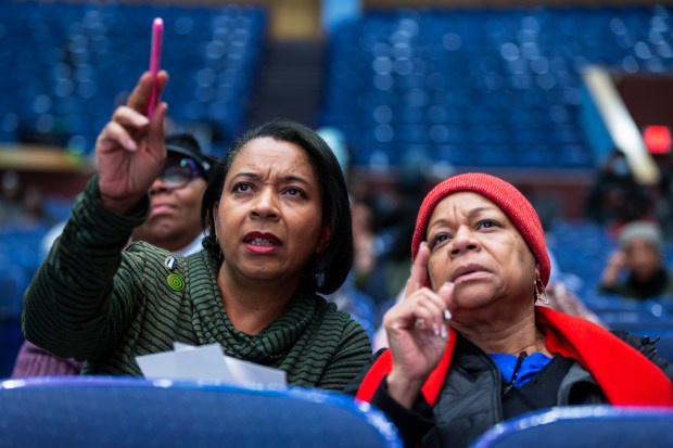 Vanessa Johnson McCoy, left, and her sister Loretta Johnson look for their unique identification number for reparations during the Evanston reparations committee meeting at Evanston Township High School on Jan. 11, 2024. About 200 people attended the meeting to see the random selection order of direct descendants who will receive $25,000 each in reparations funding. (John Konstantaras/for the Chicago Tribune)