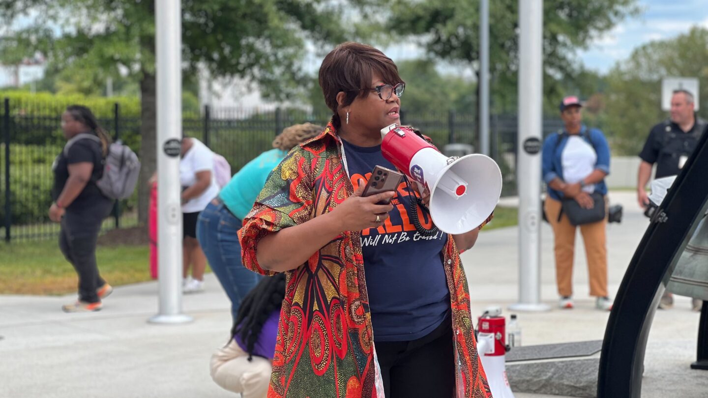 Melanie Campbell holds a megaphone in front of the Liberty Bell in Atlanta while people behind her stoop to give offerings at the vigil.