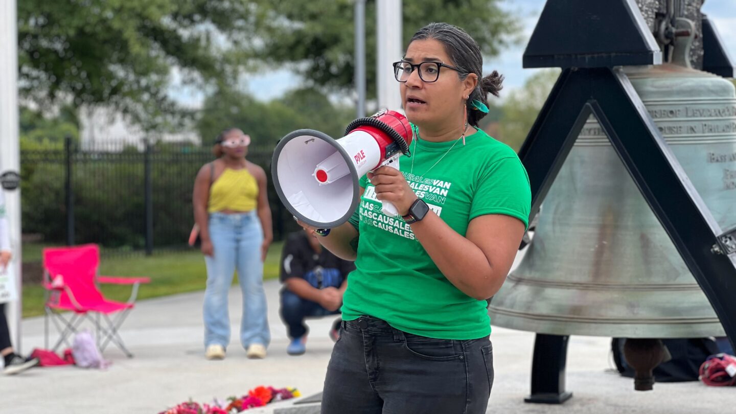 Fanny Gomez speaks into a megaphone and wears a green shirt at a rally.