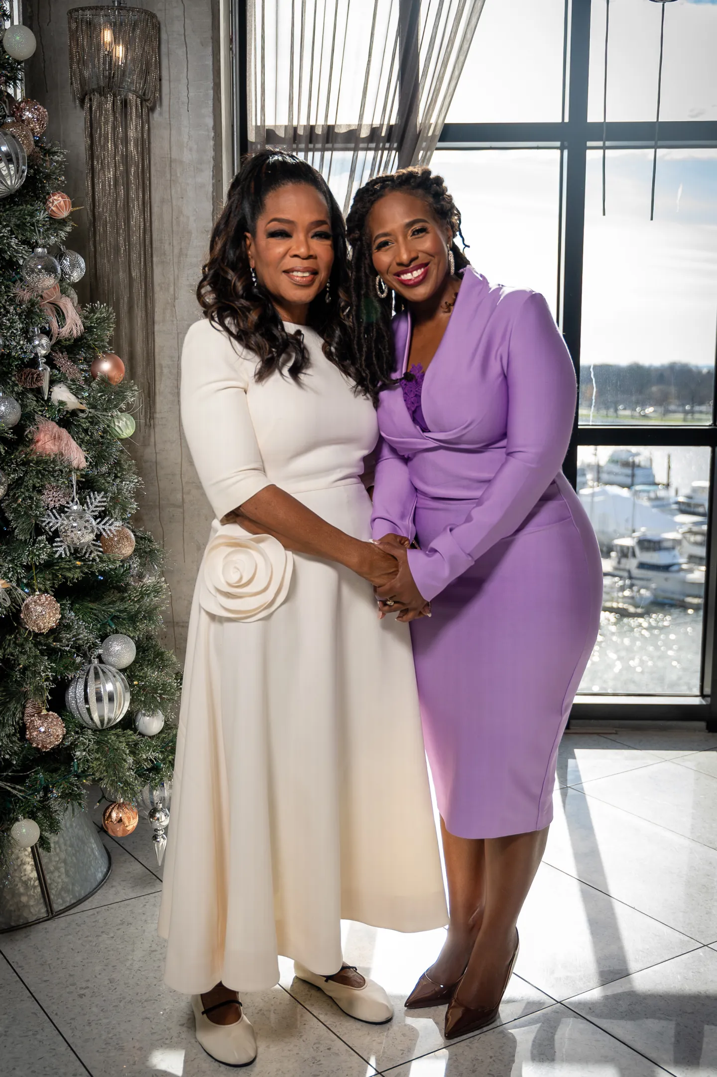 Oprah Winfrey, wearing white, holds hands with Jotaka Eaddy, Win With Black Women's founder, in purple.