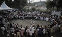 An overhead, twilight view of dozens of people in a wide circle, most of African descent and wearing white, with a man and a woman in the center.