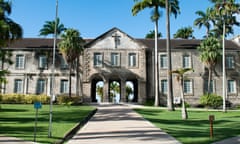 A two-storey greybrick college entranceway flanked by bright green grass, palm trees and blue sky