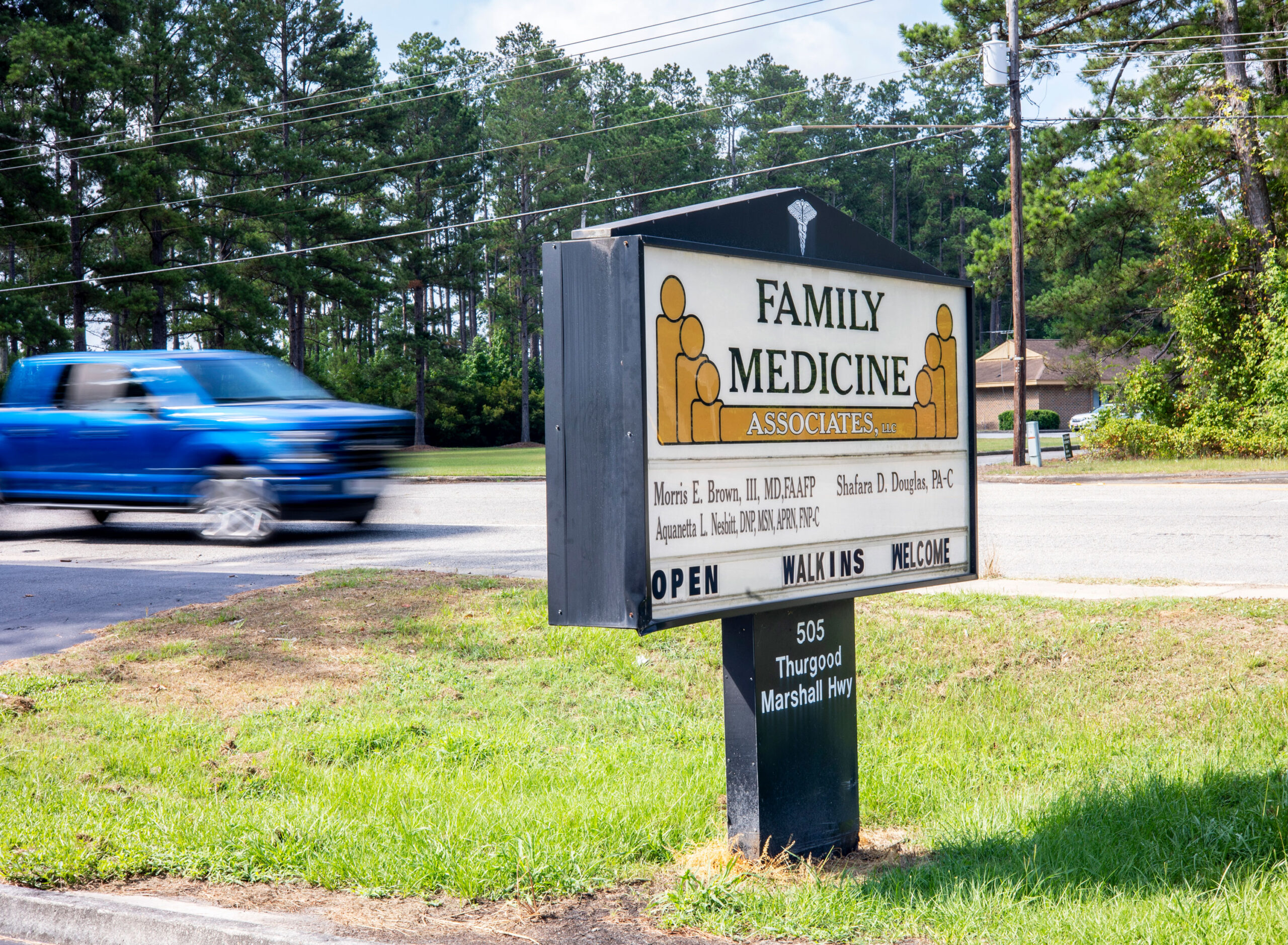 A photo of a sign for Family Medicine Associates. Behind it, a blurred blue truck drives by.