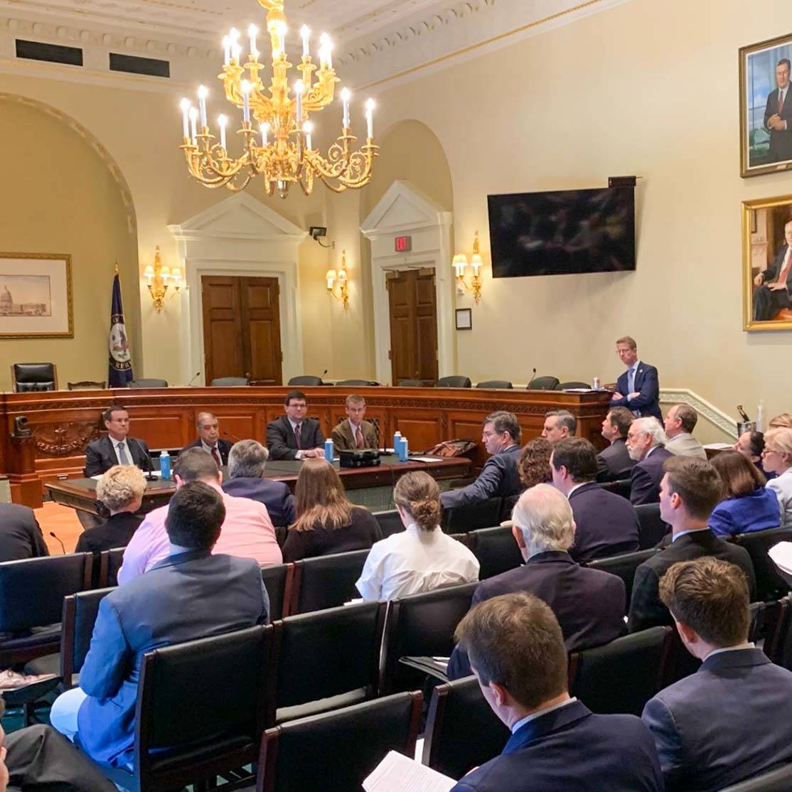 A room in Washington DC, chandelier handing in the middle above the heads of a group of seated people.