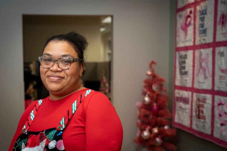 A Black woman wearing glasses and a red shirt stands for a portrait. 