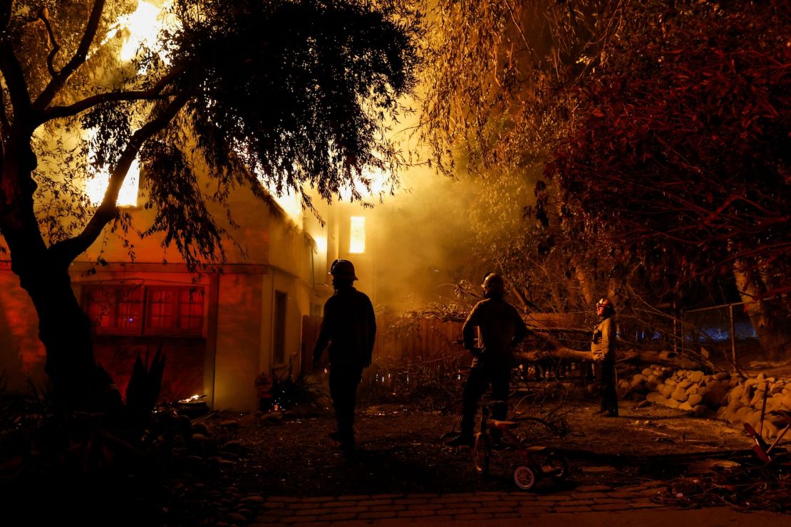 Firefighters stand near a burning house, as powerful winds fueling devastating wildfires in the Los Angeles area forced people to evacuate the Eaton Fire in Altadena on January 8.