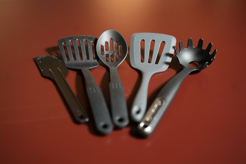 A black plastic spatula, spoon and pasta server sit on a red bench