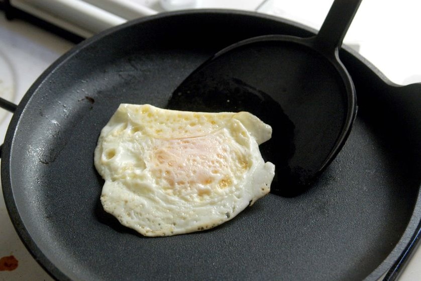 A spatula sits under a fried egg being cooked 'over easy' in a frypan